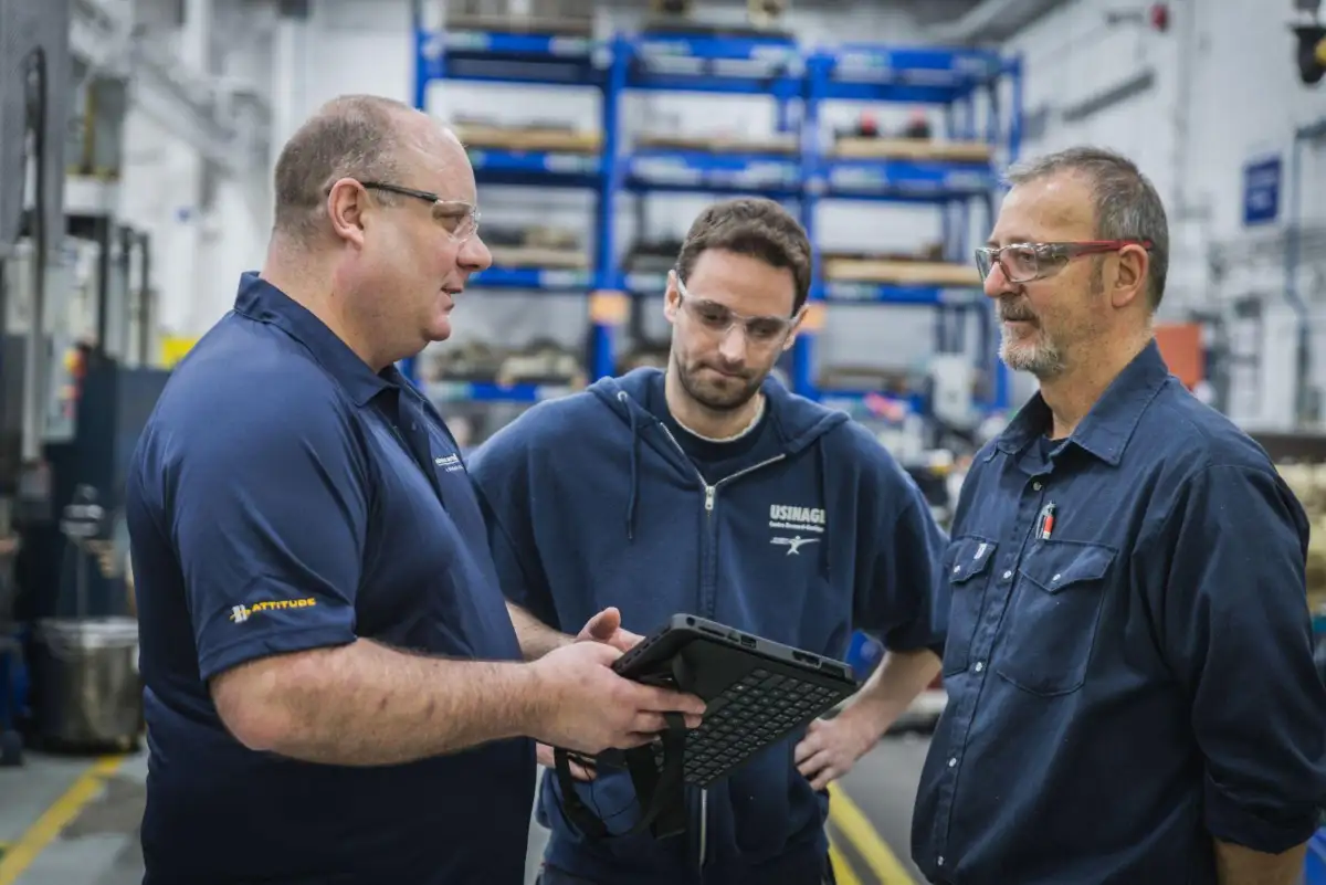 Trois personnes dans une usine qui discutent en regardant une tablette